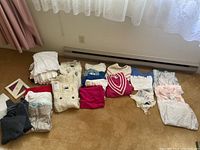 Overview of folded women’s clothing items on floor, showing variety of tops, sweaters, and undergarments in white, cream, blue, pink, red and beige colors.