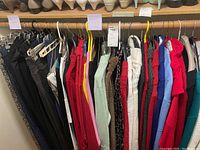 Rows of women's clothing hung on rack showing items pants and sweaters in multiple colors