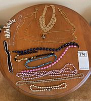Photo showing 11 assorted women's costume necklaces arranged on round wooden table, displaying a variety of styles, colors, and bead types.