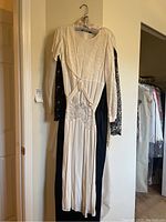 Three women's gowns hanging; front cream-colored gown has lace detail with missing sleeve detail, black lace sleeves on other gowns clearly visible