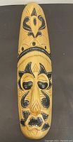 Front view of the tall wooden mask showing the full carved face and painted details.