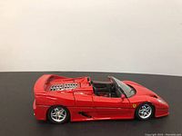 Side view of red Burago Ferrari F50 diecast model car on a black surface with closed doors and rear hood.
