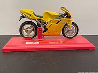 Side angle of the yellow Maisto Ducati 748 diecast model motorcycle mounted on a red display stand.