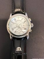 Front view of watch on black background showing stainless steel case and black leather strap