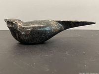 Side view of stone bird sculpture showing smooth polished surface and elongated tail.