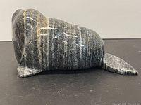 Side view of the striped dark gray stone walrus figurine showing the carved details of the flipper and tail.