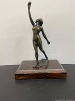 Front view of the bronze woman statue showing the figure standing with arm raised and wooden base.