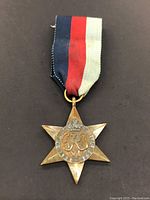 Obverse view of the six-pointed star medal with a red, white, and blue ribbon, showing a crowned 'GR VI' monogram