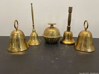 Five vintage brass bells displayed on a black surface showing various shapes and sizes.