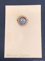 Front view of vintage pin showing sterling silver coin center and gold-tone twisted rope border.