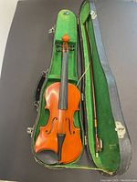 Violin laid inside open case showing front side with strings, fingerboard and chinrest