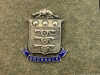 Close-up of the sterling silver pin badge showing the detailed ordnance crest with three cannons, a beaver figure on top, and blue enamel banner.