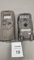 Two trail cameras side by side on a table with MaxSold lot card