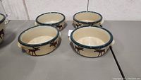 Four vintage ceramic chowder bowls shown together, beige with green rim and brown moose decoration.