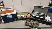 Lot contents on table including cooler, tent bag, stove, and sleeping bag