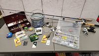 Full view of fishing rods, reels, Fenwick bucket, Frabill aerator, lure packages, tackle boxes, and fishing line on a table.