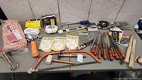 Wide view of lot showing hand tools, ropes, strap buckles and saws arranged on table.
