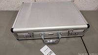 Closed silver metal briefcase from top view on gray surface.