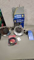 Two propane tank top heaters on a gray table, one inside its original box and the other outside with protective cages and regulators visible, plus a sealed accessory cable.