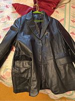Black leather blazer jacket laid flat on quilted bedspread