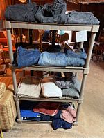Full view of plastic shelving with folded black, gray, blue jeans on top two shelves, and various tops and sweaters folded on bottom shelves.