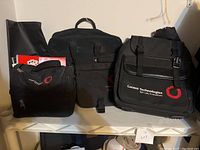 Three black Lucent Technologies branded bags in different sizes placed on a shelf.