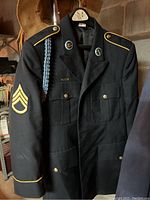 Front view of a dark military jacket featuring Sergeant chevron patch on sleeve, gold piping on cuffs and epaulets, buttons, and blue braided cord on shoulder.