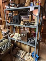 Overall view of four-tier metal shelf with vintage telephones, wooden ringer boxes, a mechanical dial timer, and push-button phones