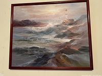 Framed oil-style painting showing rough ocean waves and lighthouse on a rocky shore, with a reddish brown wood frame.