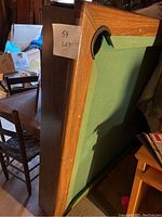 Side view of the rectangular pool table with wood frame and green felt surface, showing the corner pocket and wood grain detail.