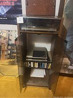 Full view of wooden stereo cabinet with glass doors open showing turntables and VHS tapes inside