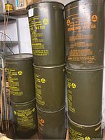 Photo of six green metal drums labeled for drinking water storage by Civil Defense