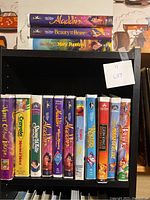 Photo showing VHS tapes including Aladdin, Beauty and the Beast, Mary Poppins, and others on a black shelf