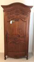 Front view of closed armoire showing carved door with decorative lock and key