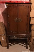 Front view of cabinet with closed wooden doors featuring ornate carvings and brass handles.