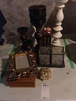 Photo showing carved wooden photo frame with scroll design, wooden dresser box underneath, brass and bronze candle holders and small fabric cushion.