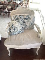 Front view of armchair with two decorative damask-patterned throw pillows on beige upholstered seat