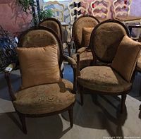 Four wood-framed armchairs with floral tapestry upholstery shown in basement setting