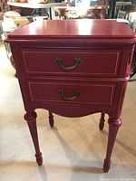 Front view of red distressed 2-drawer end table showing metal handles and decorative legs.