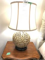 Front view of one lamp lit showing carved filigree base and cream shade
