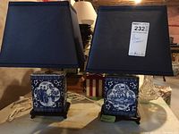 Two oriental style table lamps with blue and white ceramic bases and dark blue square shades shown side by side on table.