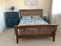 Front view of queen wooden bed with headboard, footboard, and mattress with floral bedding
