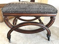 Close-up of the stool showcasing the black and white geometric patterned fabric top and dark wood curved frame with caster wheels.