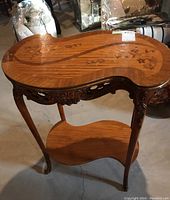 Full view of the scroll-shaped wooden side table showing top with marquetry inlay and carved apron detail.