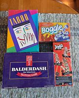 Photo of four used board games: Taboo, Boggle, Balderdash, and Jenga, displayed on a wooden table.