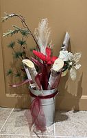 Full view of decorative birch branches, artificial plants, and red ribbon in metal bucket.