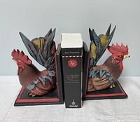 Front view of the pair of rooster bookends holding a book, showing color and carved detail.