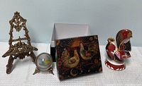 Photo showing all four items: ornate brass frame stand, glass globe with brass tripod stand, small painted decorative box with removable lid, and bone china rooster figurine.