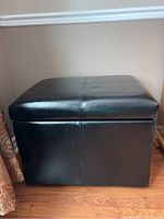 Full view of the black leather-like ottoman showing its shape and size.