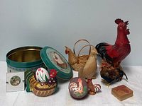Wide view of the rooster-themed knickknacks including tin, various wooden and metal rooster and chicken figures, and small decorative boxes on white surface